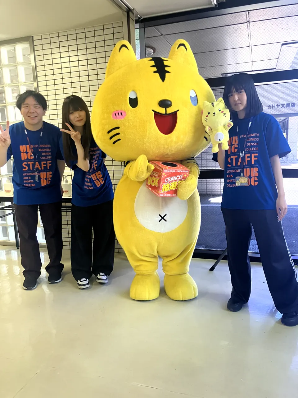 学校キャラクターと学生スタッフが写真撮影をしている様子